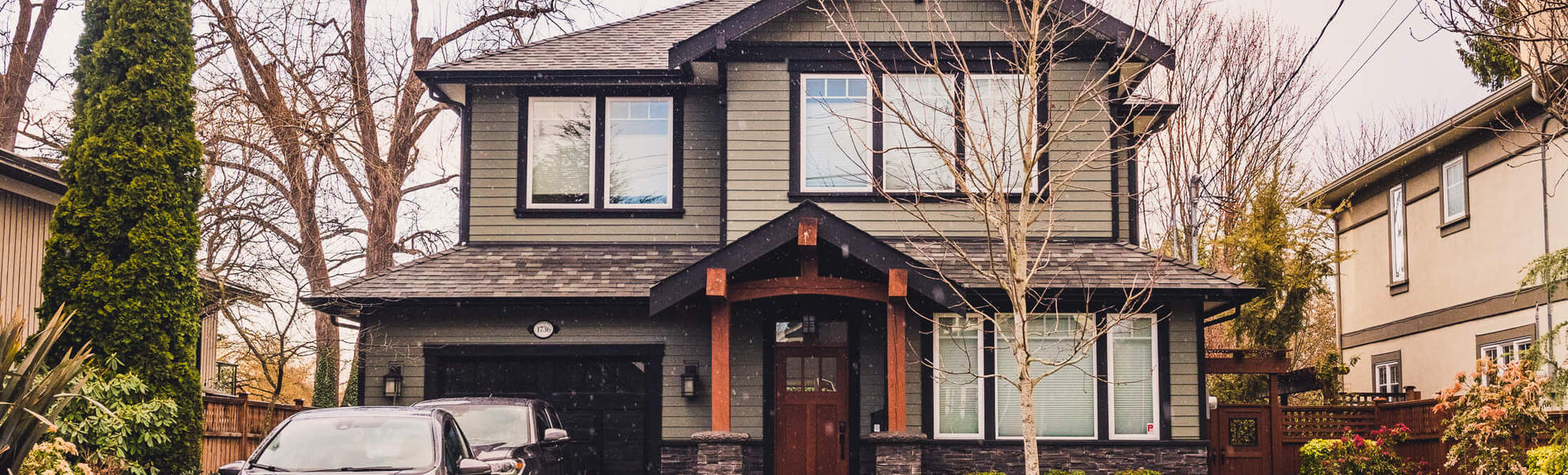 Front enterance of two story grey house with cars in the driveway