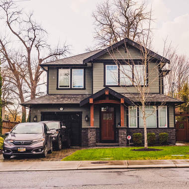 Front enterance of two story grey house with cars in the driveway